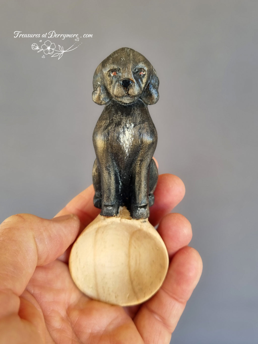 Small spoon with dog handle held in a hand against a gray background