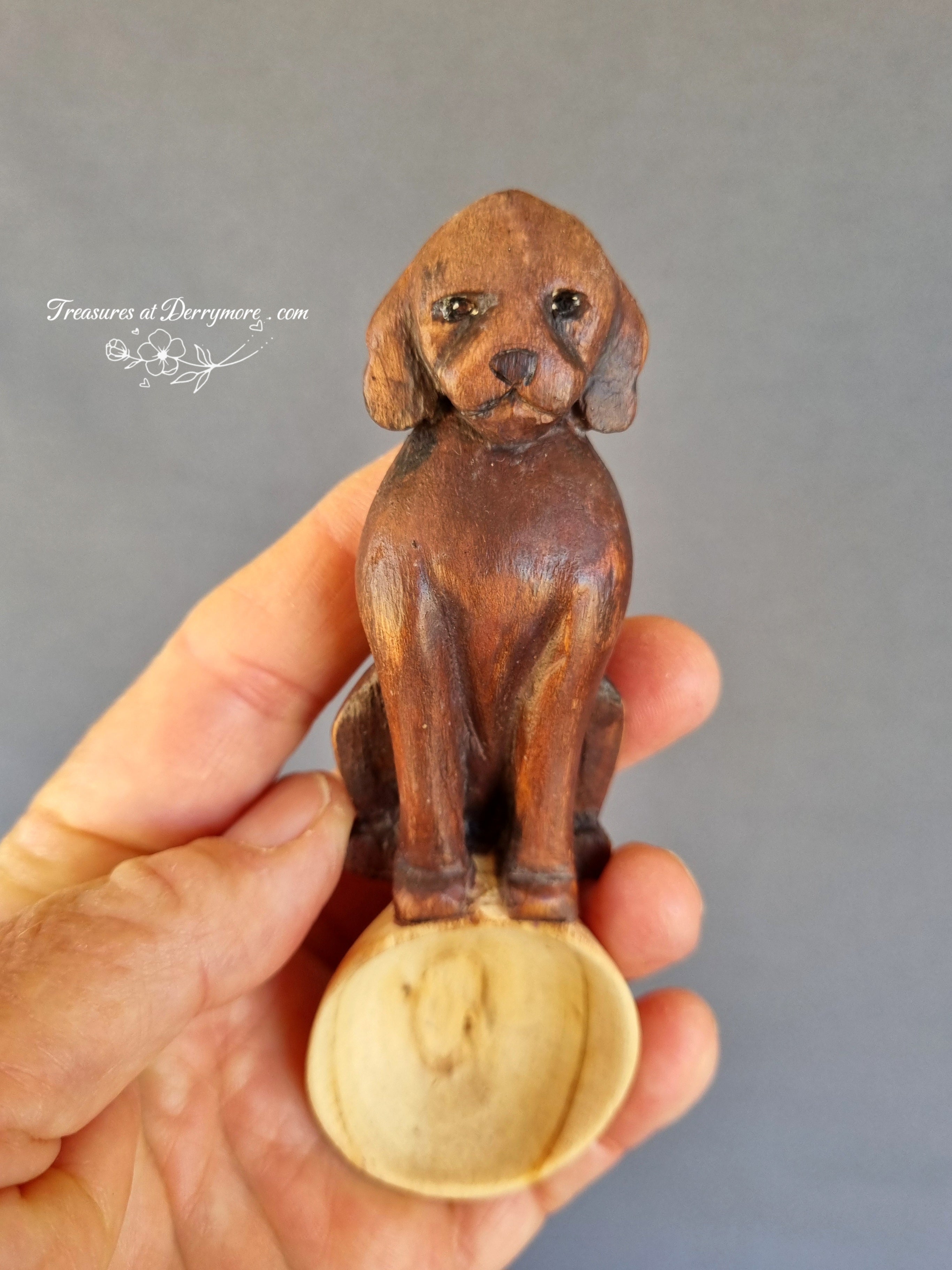 Wooden dog spoon held in a hand against a gray background