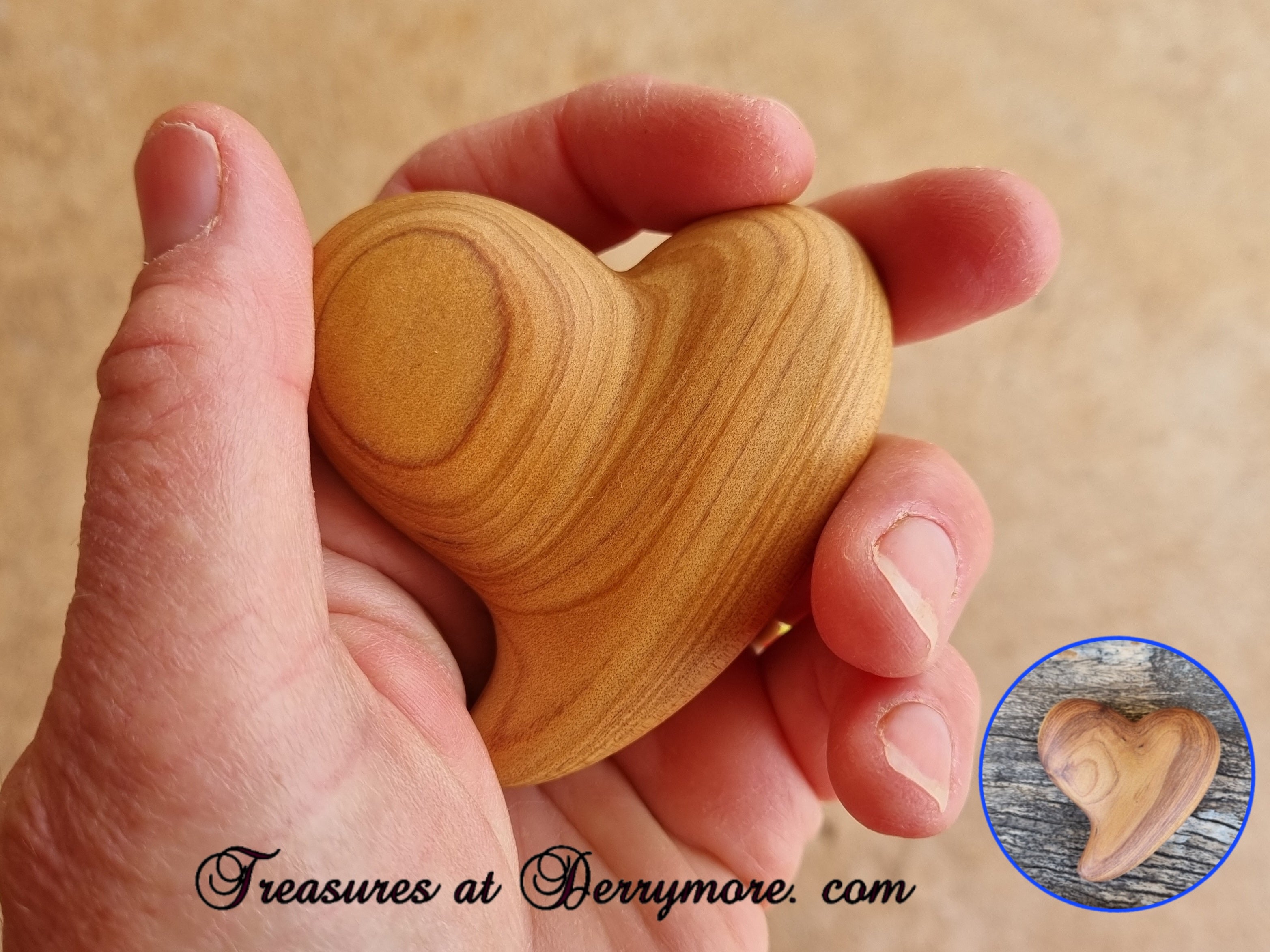 Hand holding a carved wooden comfort heart with 'Treasures at Derrymore.com' text.