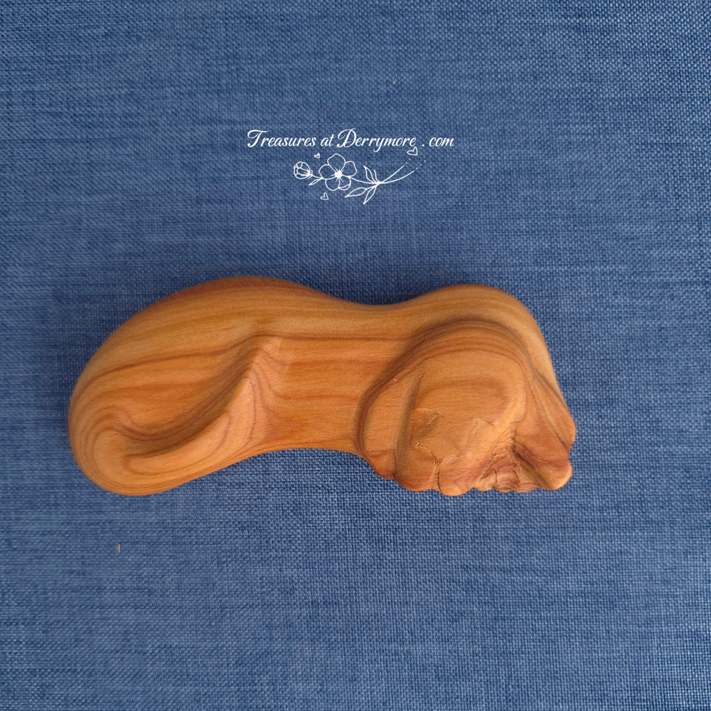 Carved Wooden dog comfort piece on a blue textured fabric background with 'Treasures at Derrymore' branding.