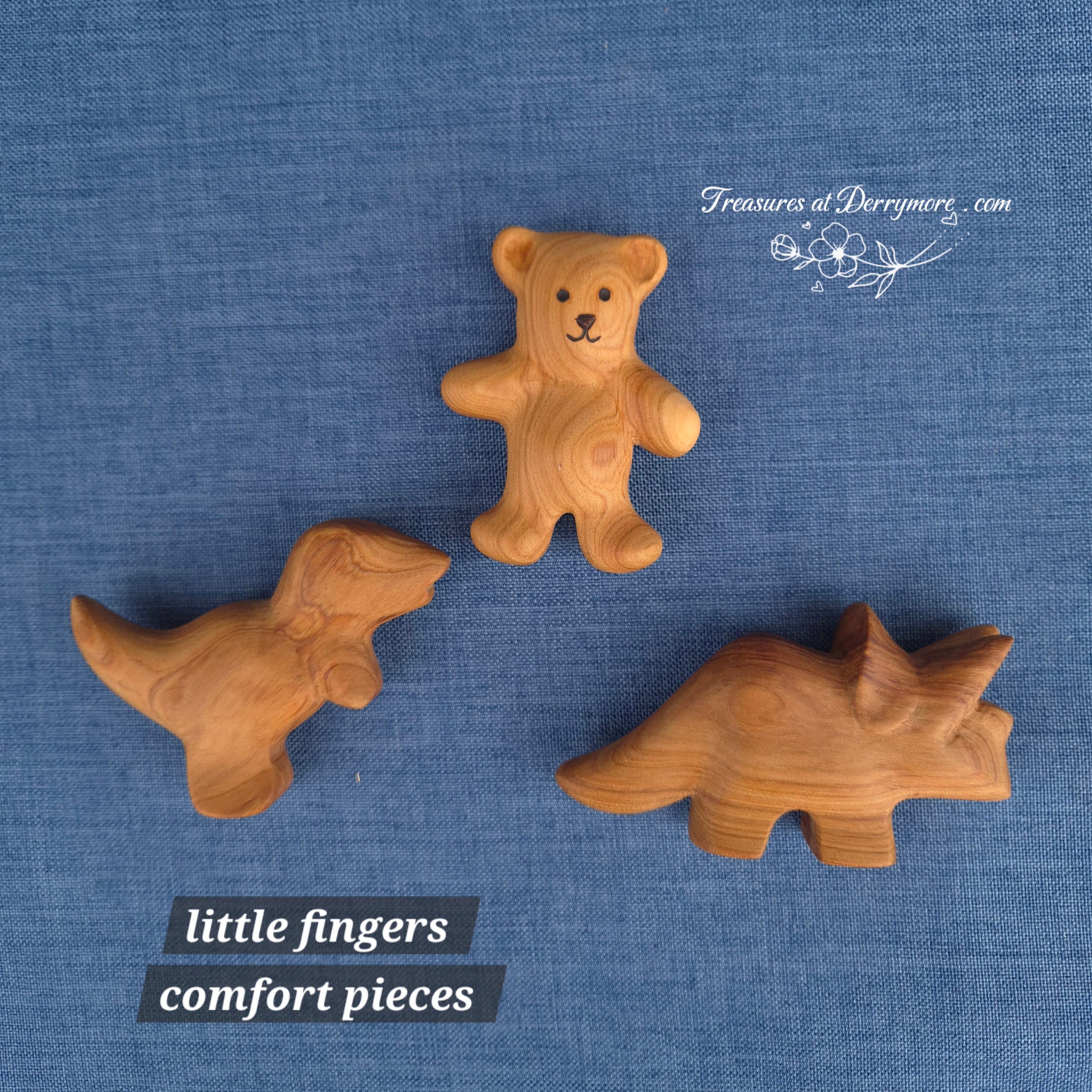 2 small carved wooden dinosaurs & 1 small carved wooden bear on a blue fabric background with 'Treasures at Derrymore' branding 