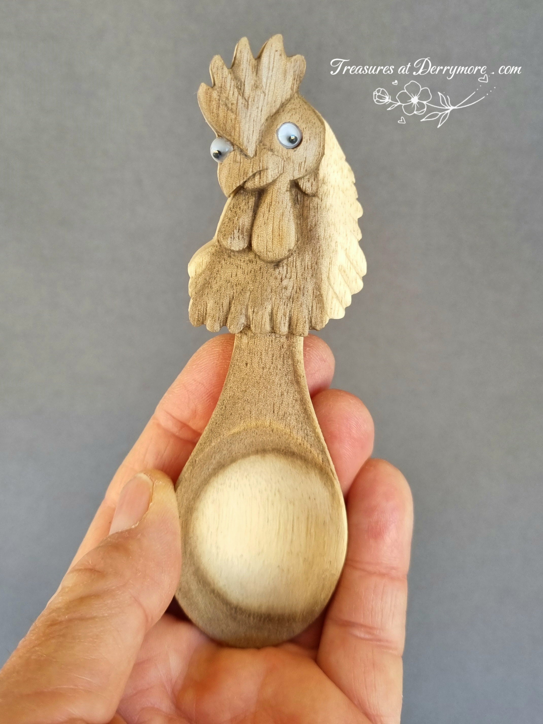 Wooden spoon with rooster design held by a hand against a gray background