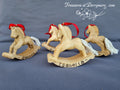 Three hand carved wooden rocking horses. Christmas decorations with red bows on a gray background, branded 'Treasures at Derrymore'.
