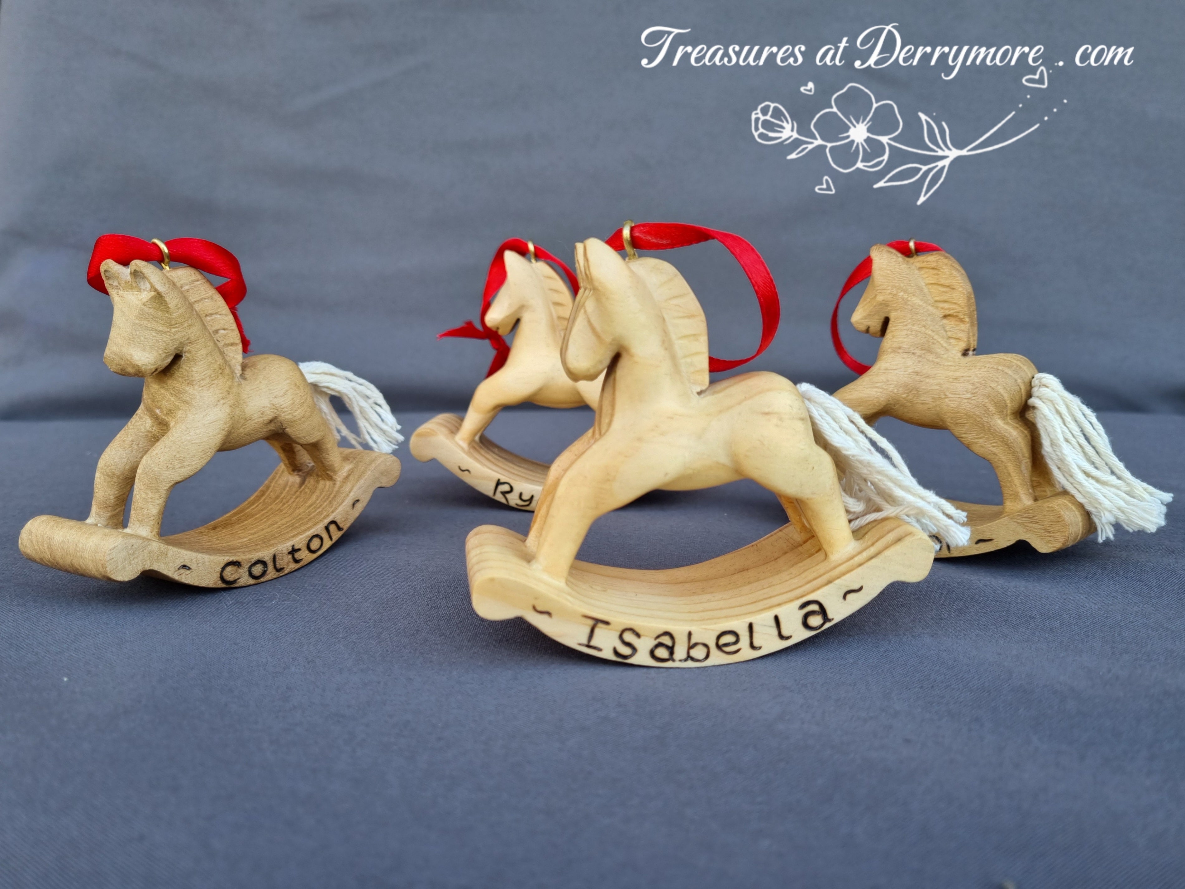 Three hand carved wooden rocking horses. Christmas decorations with red bows on a gray background, branded 'Treasures at Derrymore'.
