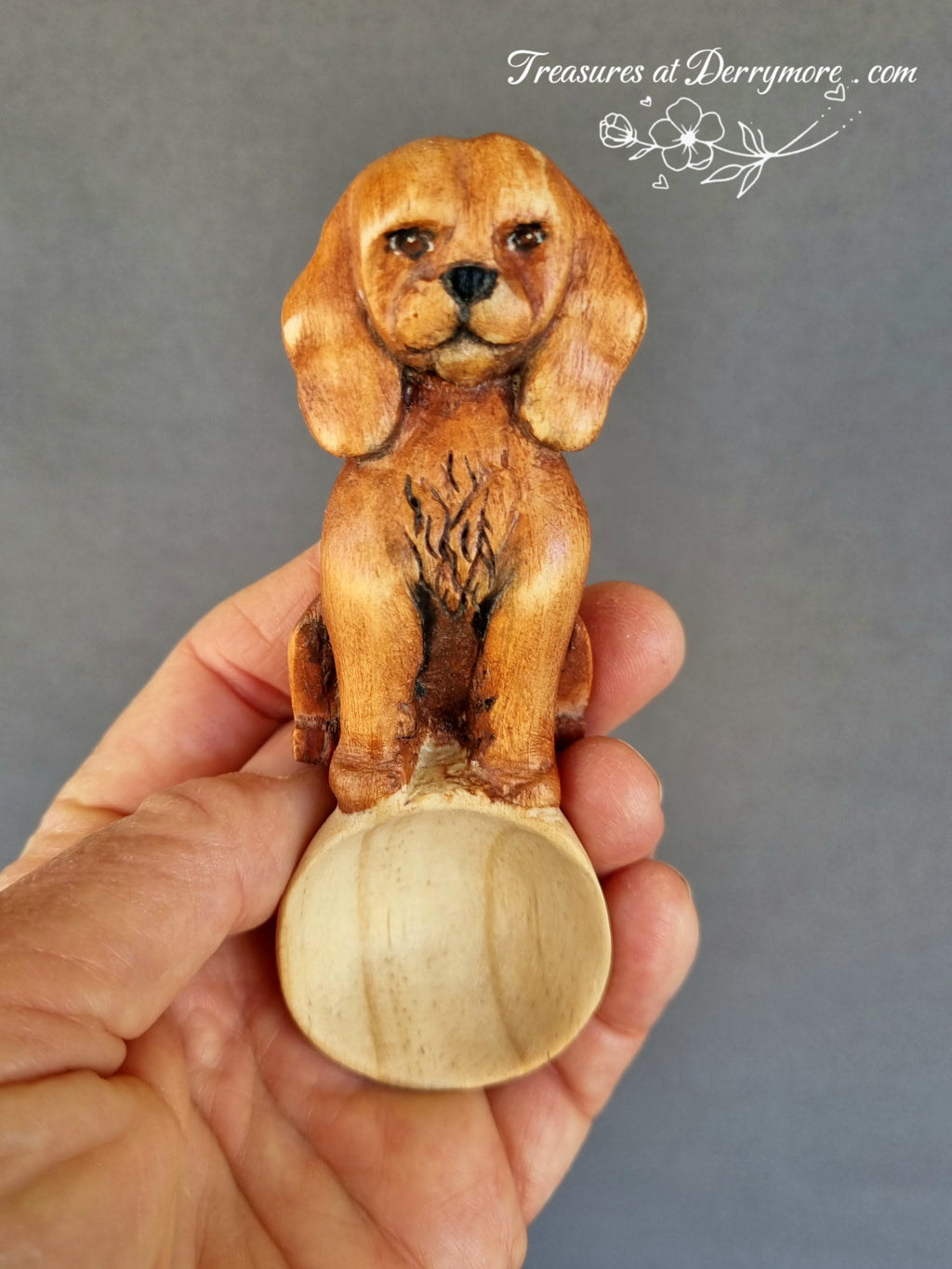 Wooden dog spoon held in a hand against a gray background