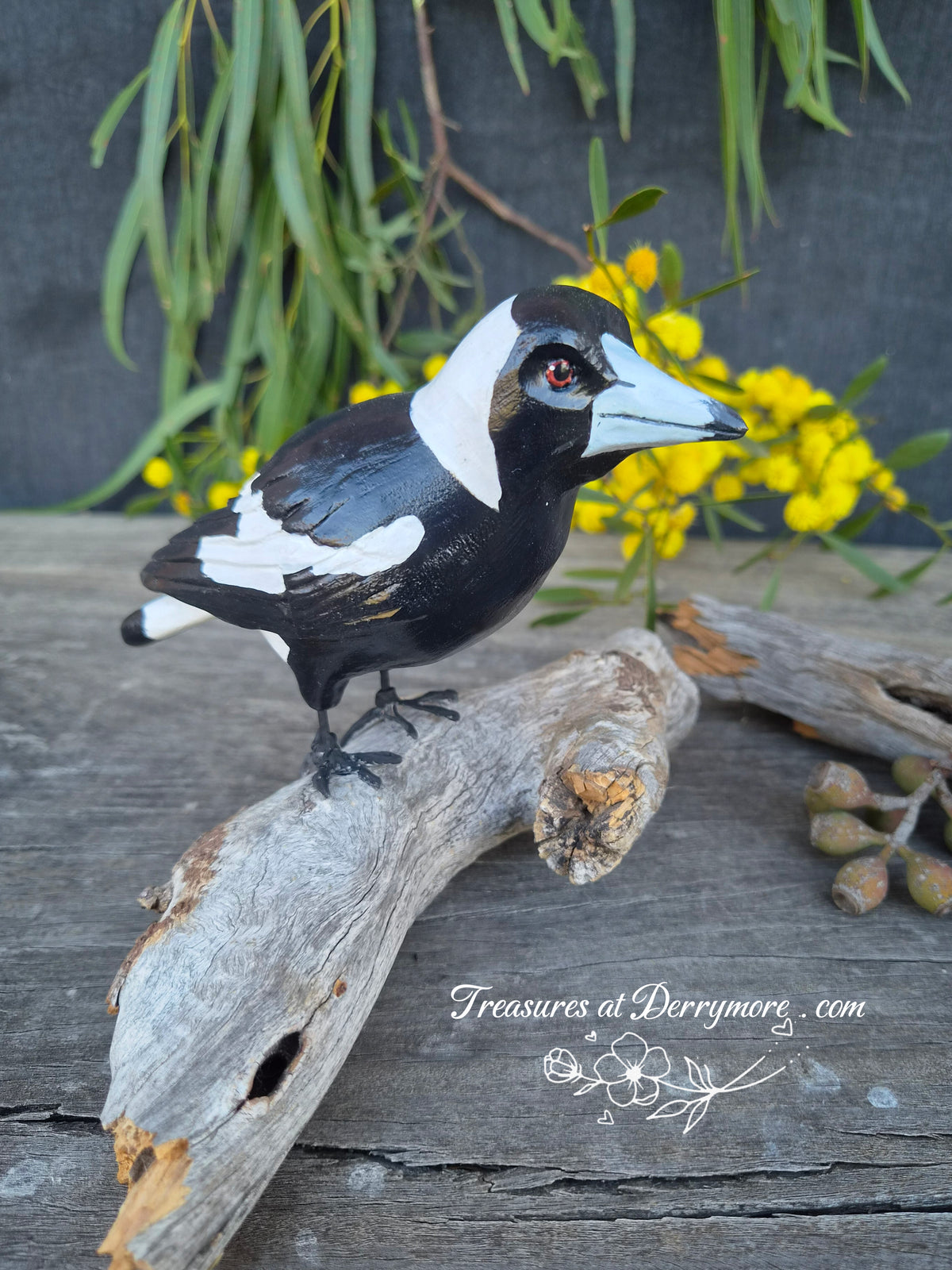 Side view of a hand carved wooden Australian magpie sculpture perched on a natural fallen piece of tree branch 